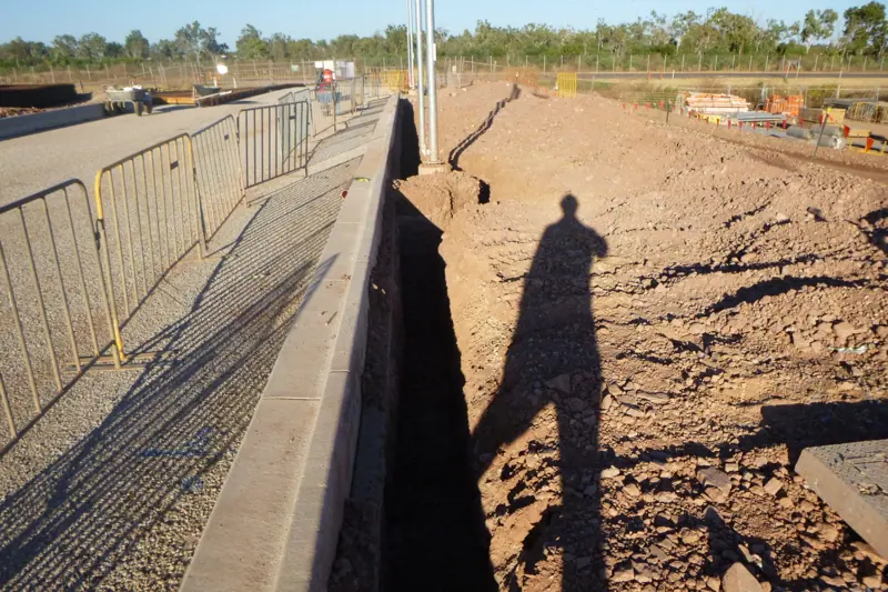 Long straight trench beside a kerb and fenceline