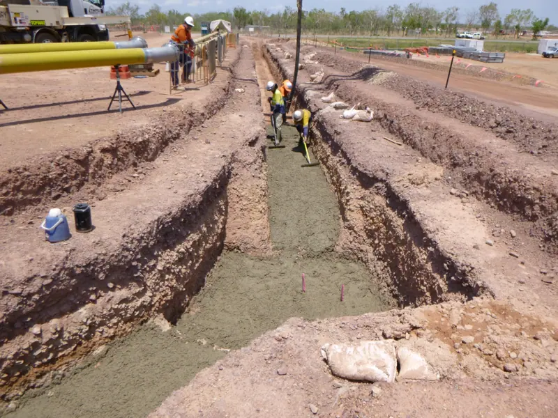Crew pouring concrete blinding in a services trench