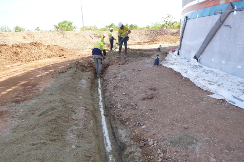 Crew hand-placing bedding sand around tank perimeter pipework