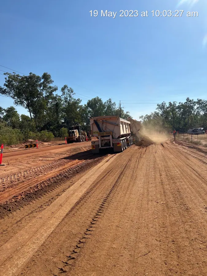 Road train side tipper discharging pavement material beside a grader