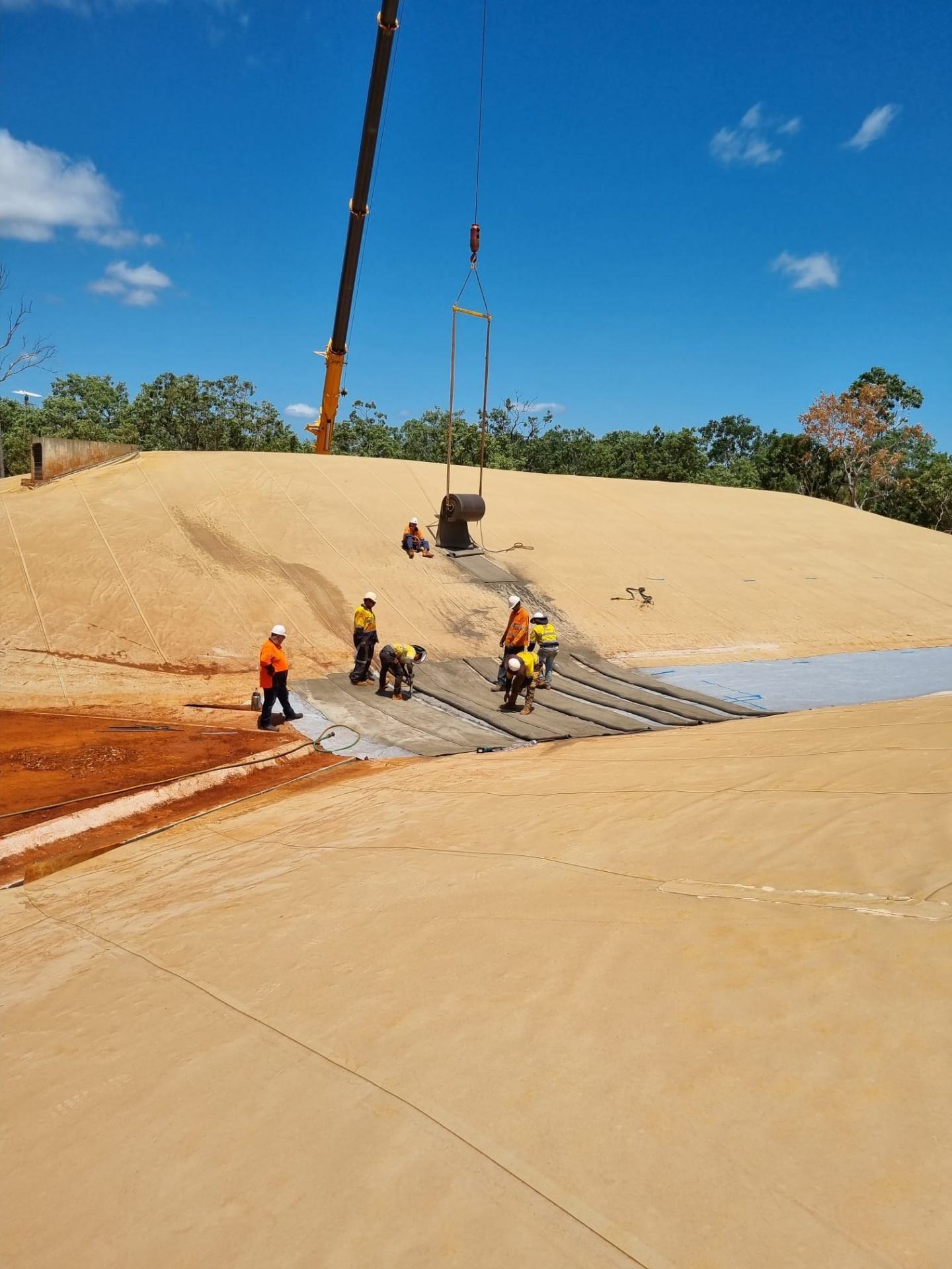 Wombarra crew lining large earthen dam wall with crane-lifted geosynthetic roll