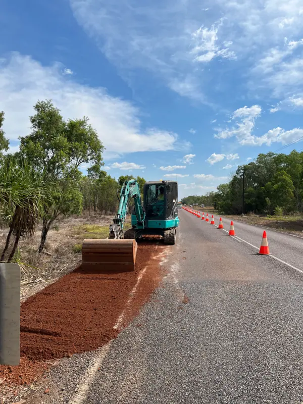 Mini excavator spreading shoulder material beside a sealed highway