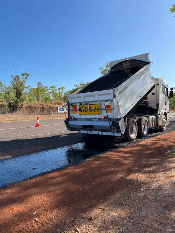 Tipper spreading sealing aggregate over freshly sprayed bitumen