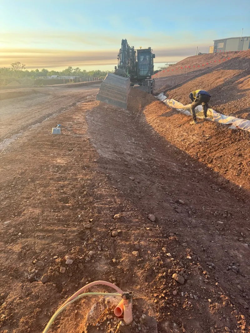 Wheeled excavator forming a batter drain at sunrise