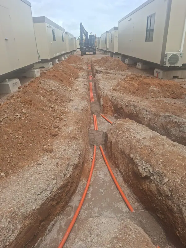 Orange electrical conduits laid in trench between accommodation units